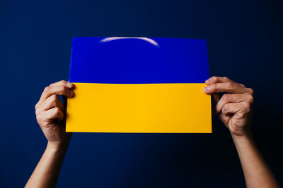 Cropped hand of woman holding paper against blue background