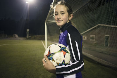 Portrait of girl with soccer ball standing against goal post