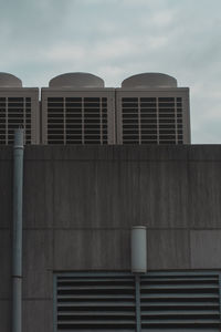 Low angle view of air conditioning system and air duct pipe on concrete building against sky 