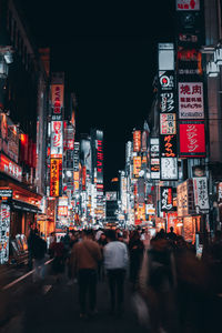 Rear view of people walking on illuminated street amidst buildings at night