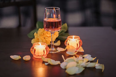 A glass of rose wine, two candles and rose petals on a dark table