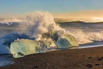 Waves breaking at beach against sky during sunset