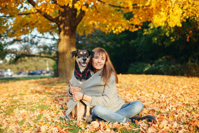 Portrait of young woman with dog sitting on leaves during autumn