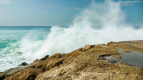 Waves splashing on rocks at shore against sky