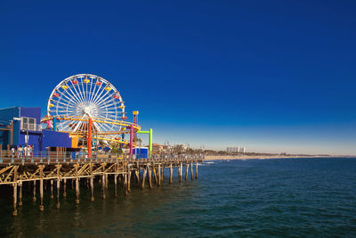 Ferris wheel at beach against clear blue sky