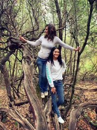 Full length of happy young woman standing on tree trunk