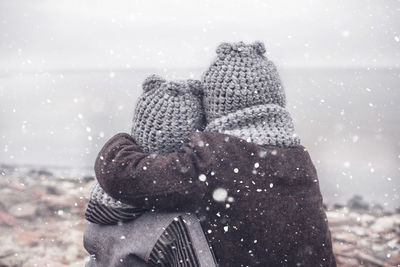 Girl in knitted grey hat hugging her frozen smaller brother