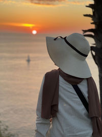 Rear view of woman standing by sea against sky during sunset