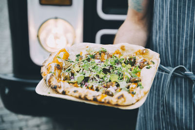 Close-up of owner holding indian food in plate against commercial land vehicle