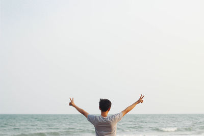 Rear view of man with arms raised against sea