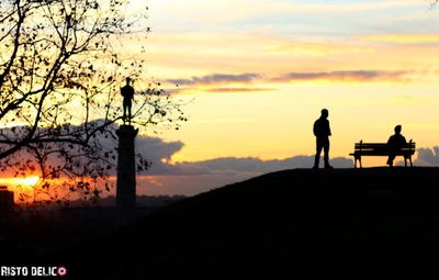 Silhouette people standing by tree against orange sky