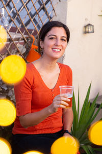 Portrait of smiling woman holding drink while sitting at outdoor restaurant