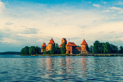 View of buildings by lake against cloudy sky