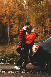 A romantic couple in love in warm sweaters is walking traveling by car in the autumn forest in fall