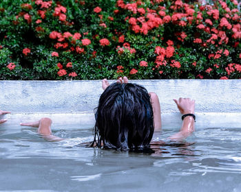 Rear view of girl swimming in pool against red flowers