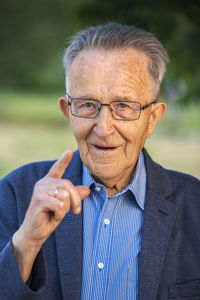 Pody portrait of an 80 old man with glasses and raised index finger and looking at  camera.
