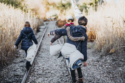 Back view of unrecognizable group of three children hiking in the woods walking in a train track