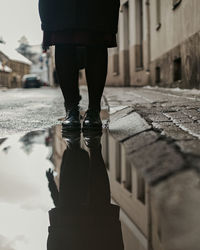 Low section of woman standing on wet footpath in city