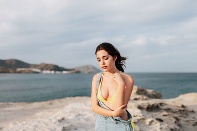 Young woman standing at beach against cloudy sky