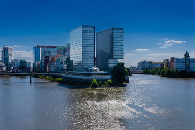 Modern buildings by river against blue sky