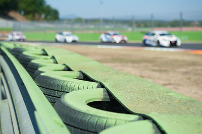 Green tires in row by railing against racecars moving on sports track