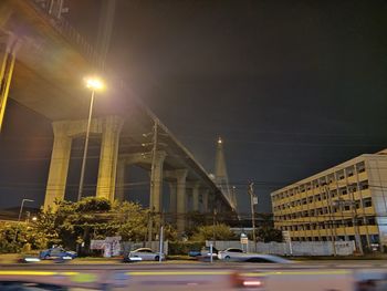 Cars on road by illuminated buildings against sky at night