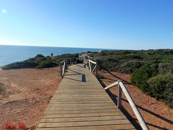 Boardwalk leading towards sea against clear blue sky