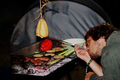 Young man preparing food over barbecue at campsite