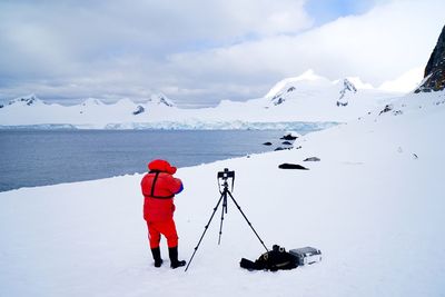 Rear view of man with by camera on tripod standing at snowcapped mountain