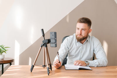 Young bearded businessman working in office sitting at table using smartphone