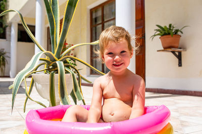 Cute child has fun in inflatable pool with toys in summer in backyard.