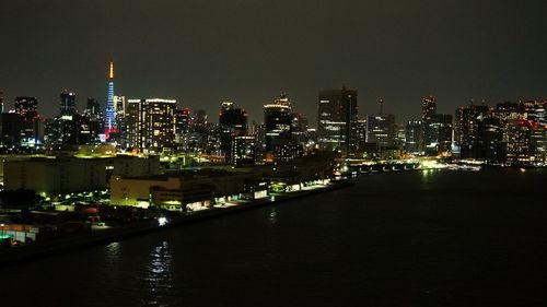 Illuminated buildings by river against sky in city at night