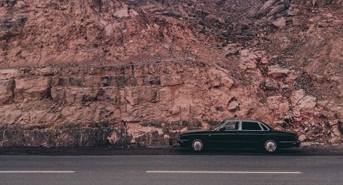 Side view of a car on road against rocky wall