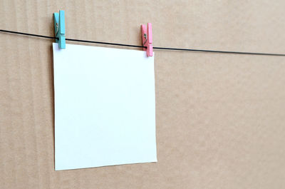 Close-up of blank paper hanging on clothesline against wall