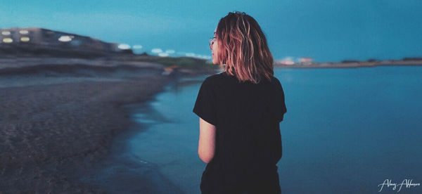 Rear view of woman standing at beach against sky