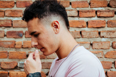 Thoughtful young man against brick wall