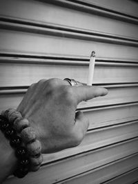 Cropped hand of man holding cigarette against shutter