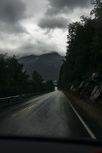 Road by trees against sky seen through car windshield