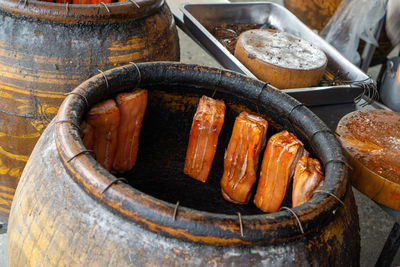 Chunks of crispy pork belly hanging inside a charcoal barbecue ceramic pot in a restaurant kitchen