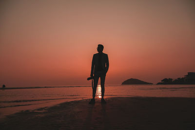 Rear view of silhouette man standing on beach during sunset