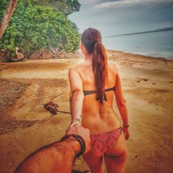 Rear view of shirtless young woman standing on beach against sky