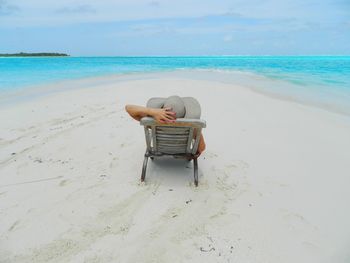 Man sitting on seat at beach against sky