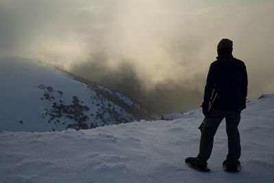 Rear view of man standing on snowcapped mountain against sky