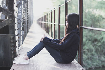 Side view of sad woman sitting on bridge