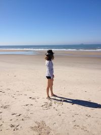 Side view of woman standing at beach against clear blue sky