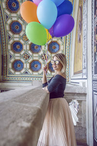 Portrait of happy young woman holding balloons at historic place
