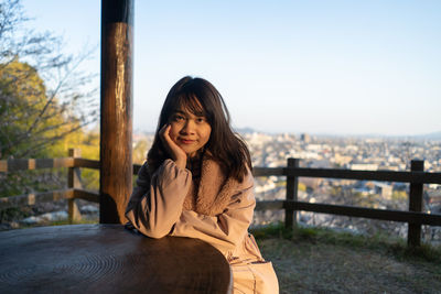 Portrait of smiling young woman sitting against railing