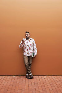 Bearded man leaning on wall while using smartphone by office building