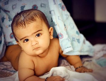 Portrait of cute shirtless baby boy lying on bed at home