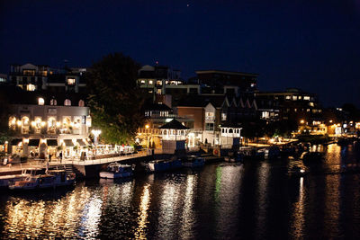 Illuminated buildings by river against clear sky at night